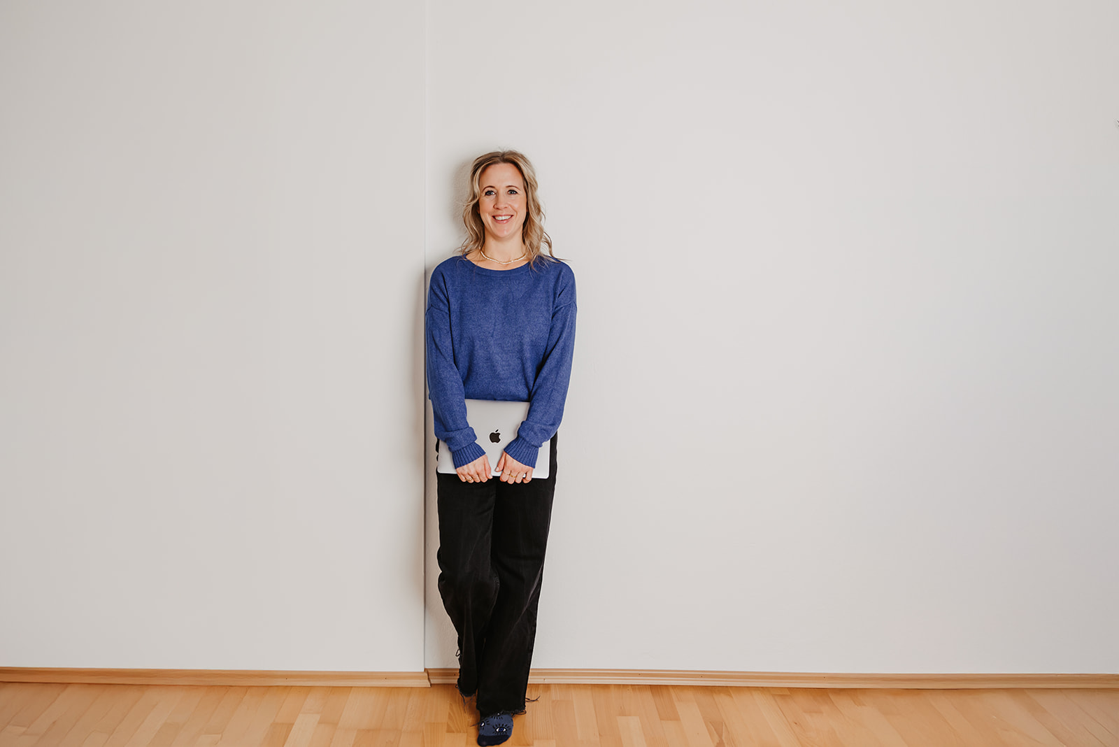 Lisa Weickl steht an einer Wand und hält einen Laptop in der Hand.
